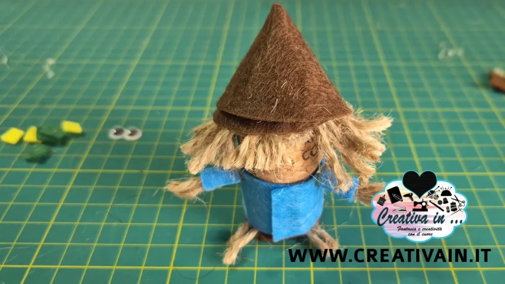 Assemblaggio dello spaventapasseri fai da te con cappello in pannolenci marrone e giacca azzurra.